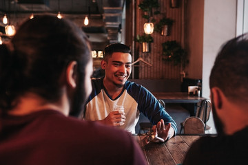 Group of mixed race young men talking and laughing in lounge bar. Multiracial friends having fun in cafe