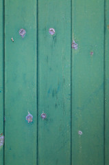 A close-up of a faded green painted door with paint flaking from the knots. Rustic textured background or flat lay concept.