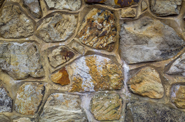 A close-up of an ornate sandstone wall made up of random shapes and sizes of stones. Rustic textured background or flat lay concept.