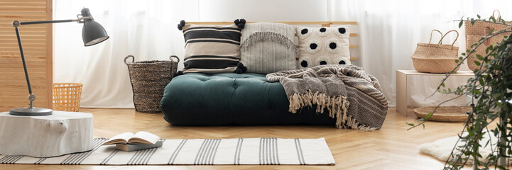 Dark green futon mattress with cushions in real photo of bright living room interior with...