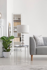 Elegant white lamp on small silver table next to grey sofa in spacious new york's style living room