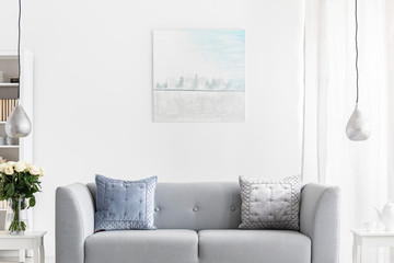 Abstract painting on the wall of luxury living room with grey couch and silver lamps above white furniture