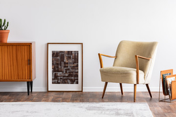 Abstract graphic in wooden frame between retro cabinet with plant and elegant beige armchair, real...