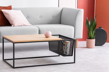 Closeup of modern wooden and metal coffee table next to stylish grey couch in trendy living room