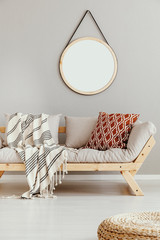 Round mirror in wooden frame on the wall of bright beige living room with comfortable sofa with...