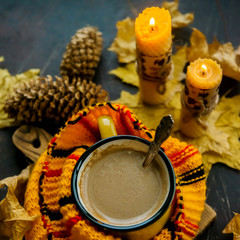 Yellow mug with autumn leaves, a book and candles. The concept of comfort and warmth. Square framing.