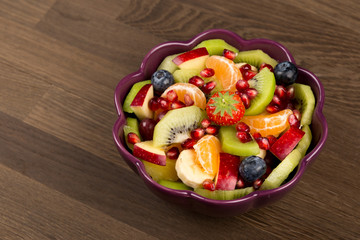 Fruit Salad in purple Bowl on wooden Table, Top View. copy space.