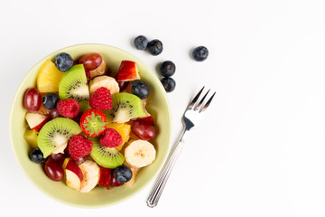 Fruit Salad in Green Bowl, blueberries and fork on white Table, Top View. copy space.