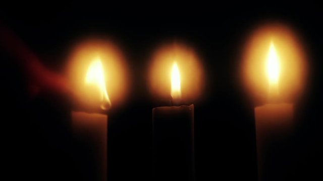 Person lit four candles with a match.  Close up on burning candles moving slowly in a circle.