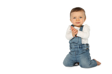 Kleinkind mit Latzhose bekleidet kniet auf weißem Untergrund