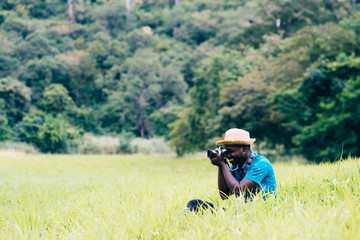 Naklejka na ściany i meble African man travelers take photo and smile happily among green meadows.
