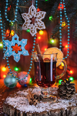 Christmas gingerbread shaped as snowflakes for Christmas-tree decorations hang on Christmas-tree branches next to a glass of mulled wine in the light of the Christmas lights in the background