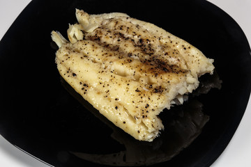 Boiled cod on a black dish. Dietary food. Delicatessen.