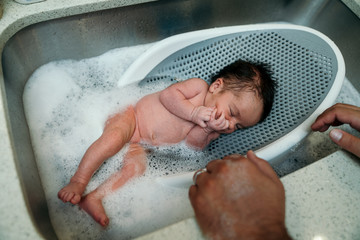 Baby girl having a bath in a basin in kitchen sink