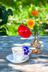 Porcelain cup of tea and beautiful spring flowers in vase on a wooden table in the garden. Summer party.