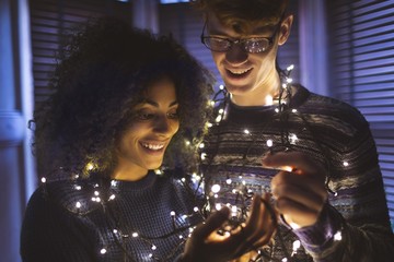 Smiling couple playing with fairy lights at home