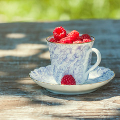 Fresh ripe raspberries and an old porcelain cup with a saucer on a wooden table in the garden.