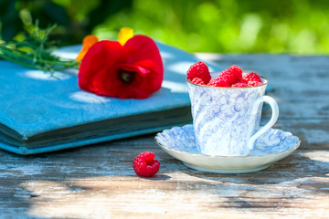 Fresh ripe raspberries and an old porcelain cup with a saucer on a wooden table in the garden.