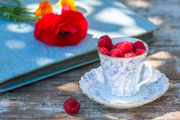 Fresh ripe raspberries and an old porcelain cup with a saucer on a wooden table in the garden.