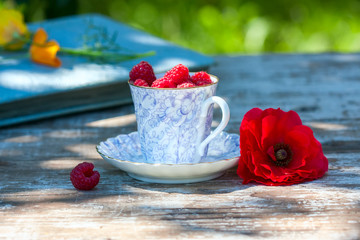 Fresh ripe raspberries and an old porcelain cup with a saucer on a wooden table in the garden.