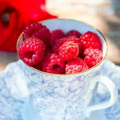 Fresh ripe raspberries and an old porcelain cup with a saucer on a wooden table in the garden.