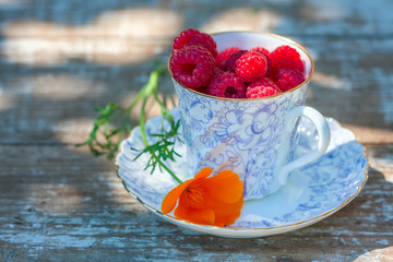 Fresh ripe raspberries and an old porcelain cup with a saucer on a wooden table in the garden.