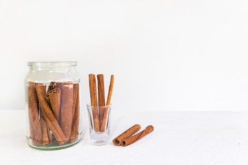 Cinnamon in glass and cinnamon sticks on white wooden table and white background, image with copy space.