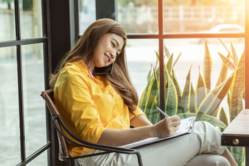 Beautiful Attractive Asian Business woman writing down requirement to book and talking with...