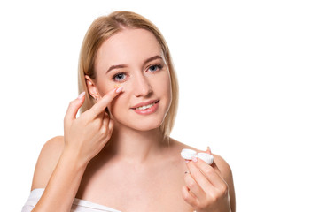 Young woman holding contact lenses cases and lens in front of her face on white background
