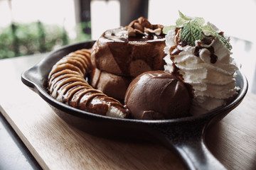Delicious pancake with banana chocolate and vanilla ice cream on black iron pan over cock coaster.