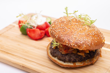 Fast food. Tasty burger with  tomato and cucumber salad on a wooden board.
