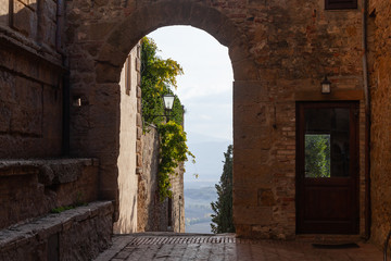 View of Tuscany hills from a medieval Pienza street where walls of old houses are twined an ivy, Italy