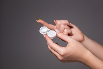 Contact eye lens. Close-up of woman hands holding white eye lense container. Woman fingers holding...