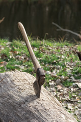 An old vintage ах with wooden handle stuck in a log against the green grass and forest background