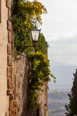 View of Tuscany hills from a medieval Pienza street where walls of old houses are twined an ivy, Italy