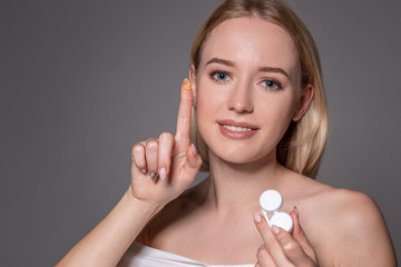 Portrait of young beautiful woman with natural makeup and contact eye lens in hand. Close-up of female model holding white lens box.