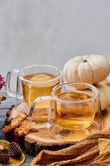 Two transparent cups of tea on a wooden cut with an orange napkin and pumpkins on the background. close up