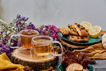 Obraz na płótnie Canvas two glass cups of tea on a wooden saw, with cookies and dried flowers on the background. wooden background. autumn tea composition. close-up