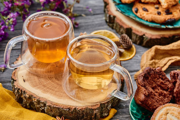 two glass cups of tea on a wooden saw, with cookies and dried flowers on the background. wooden background. autumn tea composition. close-up