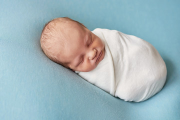 Cute newborn baby lies swaddled in blue blanket. Baby goods packaging template. Closeup portrait of newborn baby with smile on face. Healthy and medical concept. Eco conception. Nursery.