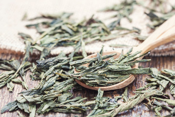 Spoon of dried green tea leaves on wooden background