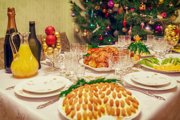 Served table with festive dishes near beautiful decorated Christmas tree in living room interior. Concept of new year holiday at cozy home. Vintage tone
