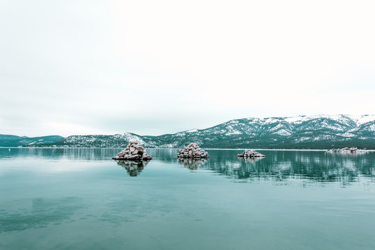 Piles of rocks in the middle of the water with snow covered mountains in the distance