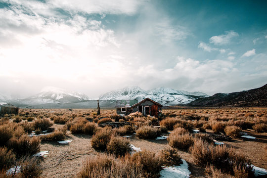 Small house in a field with snow covered mountains in the distance