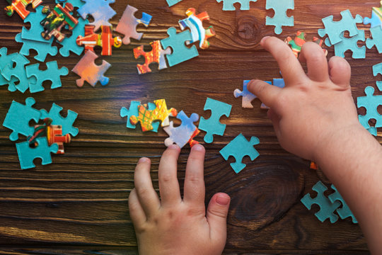 puzzles, the child's hand on wooden background. logical game, thinking, education.