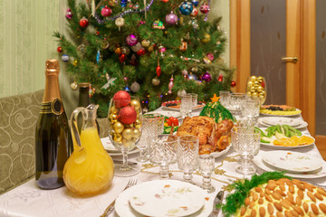 Served table with festive dishes near beautiful decorated Christmas tree in living room interior. Concept of new year holiday at cozy home