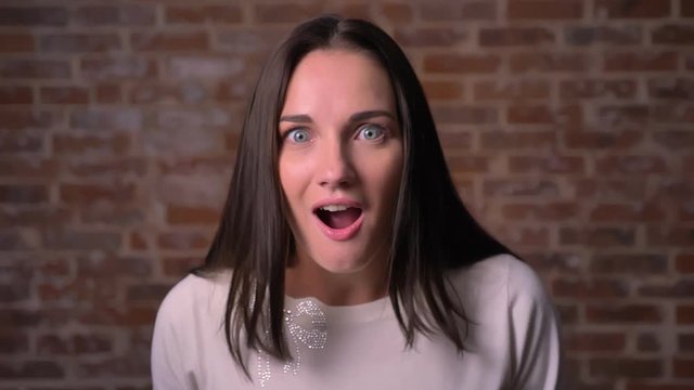 Woman watches into camera with strong positive shock on a bricken background