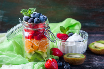 Healthy homemade fruit salad in a jar on rustic wooden background.
