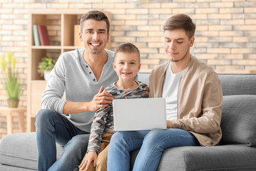 Male gay couple and adopted boy with laptop on sofa at home