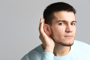 Fototapeta premium Young man with hearing problem on grey background